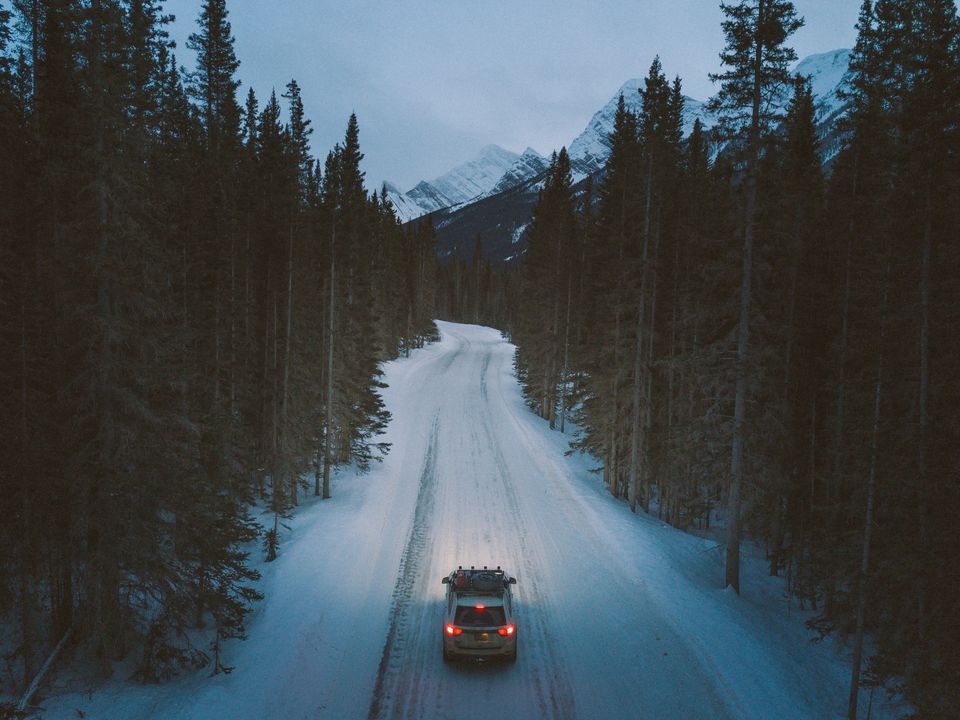 Aerial view of a car driving a snowy road through dark pine forest