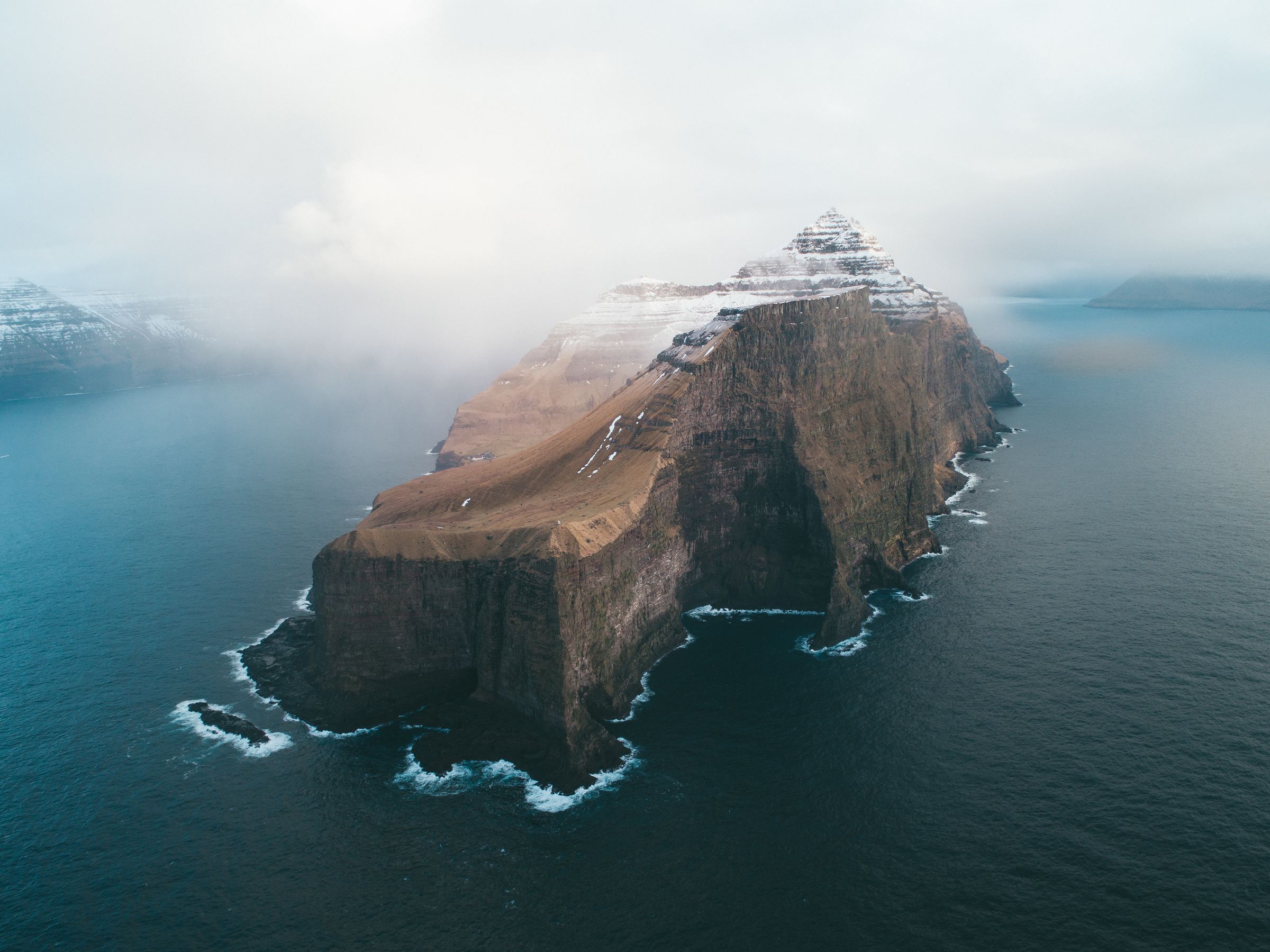 Aerial view of a cliff-sided island wrapped in fog on a dark sea