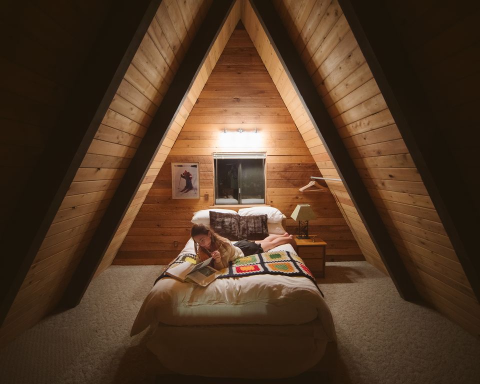 A warm, lamplit bed inside the steep wooden walls of an A-frame cabin