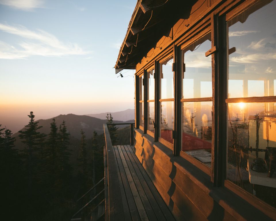 A wooden fire lookout glowing at sunset above forested ridges