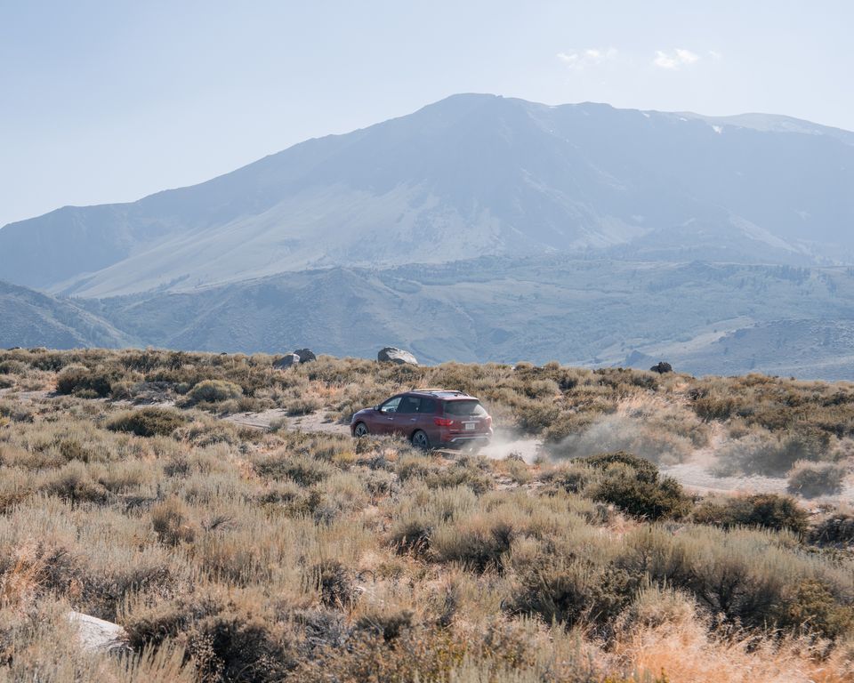 An SUV kicking up dust on a desert trail below big mountains
