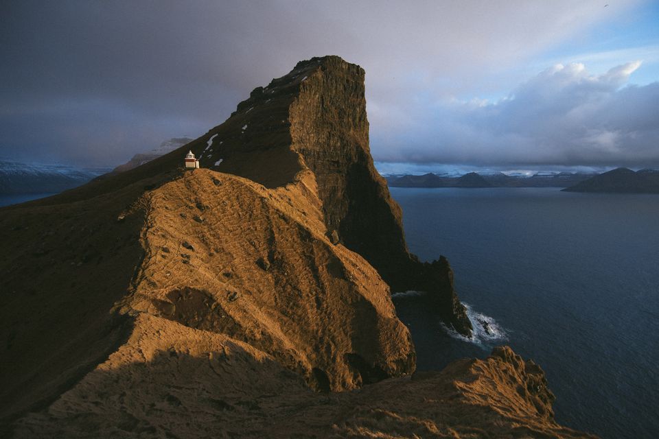 A golden grassy ridge rising to a sea cliff under dark clouds