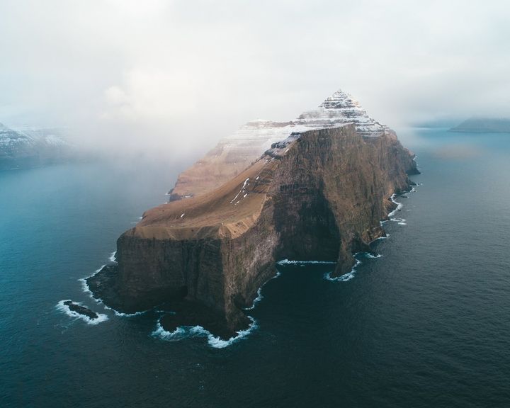 A cliff-sided island in the sea with cloud spilling over its top