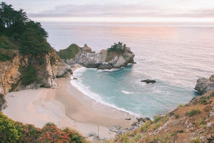 A sandy cove with turquoise water and rocky headlands at sunset