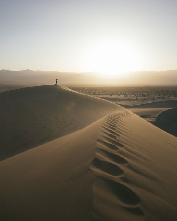 A line of footprints along a sand dune ridge as the sun sets