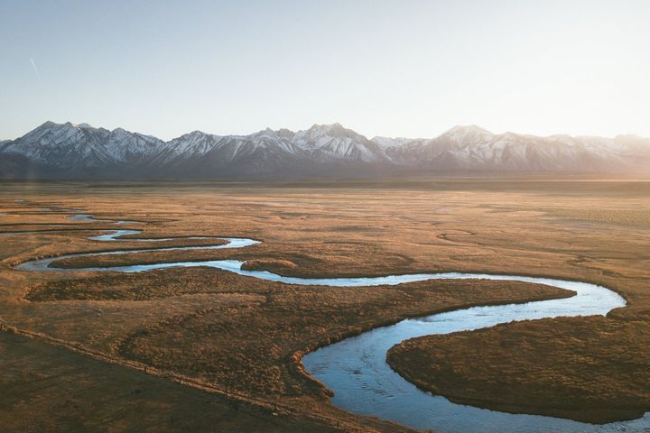 A river winding through golden grassland below snowy mountains