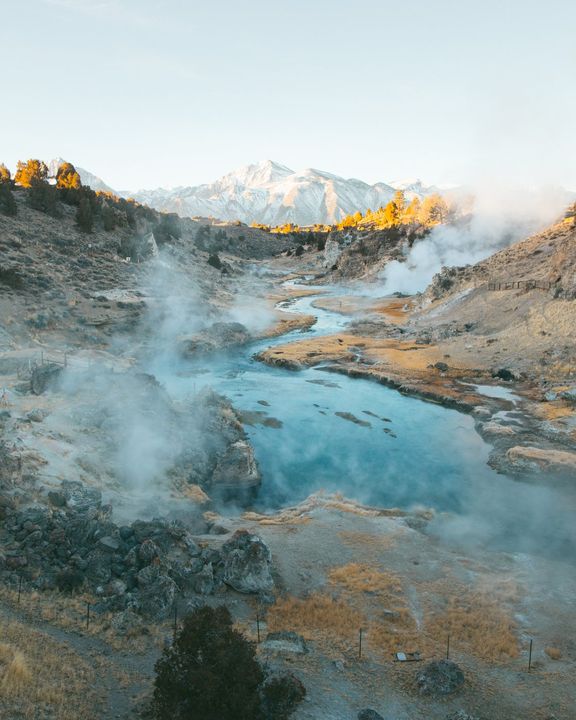 Steam rising off bright blue hot springs below a snowy peak